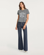 Person wearing a gray graphic T-shirt with “Cowgirls Do It Better” text and dark denim pants on a plain background.
