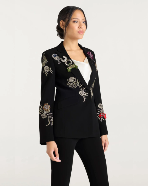 Woman wearing a black blazer with floral embellishments against a white background. 