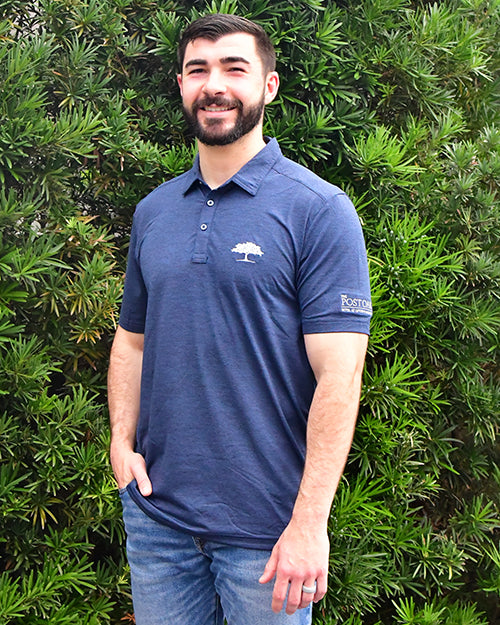 Man wearing Heating Up Golf Polo in navy in front of bush/tree background.