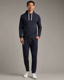 Person wearing a navy pullover hoodie and matching navy jogger pants with white drawstrings and white sneakers in a studio setting.