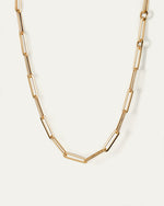 A close-up image of a gold chain necklace with elongated links. The chain features a pattern of alternating single small round links and longer rectangular links with rounded edges. 