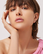 Model wearing Sylvie hoops, one hand on her face.