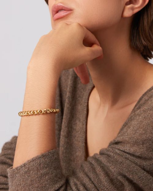 Image of a woman with her left hand under her chin wearing a gold thick twisty braided bracelet