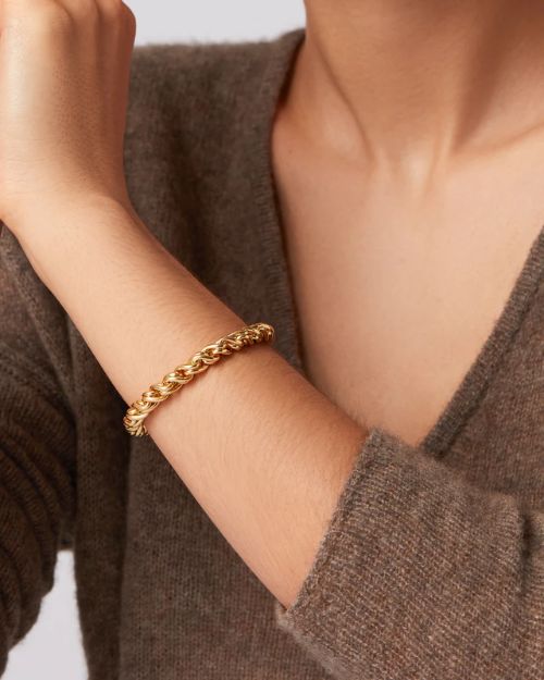 Image of a woman's left arm wearing a gold thick twisty braided chain bracelet