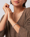 Up close picture of a woman with her arms up by her chin wearing on her left wrist a silver twisty braided bracelet