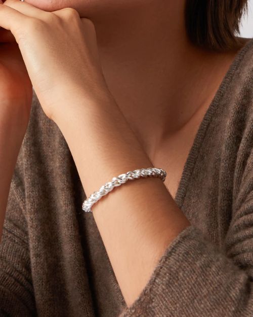 A close-up image of a woman from her chin to her elbow.  The woman has her left hand under her chin showing the silver twisty braided bracelet on her left wrist.