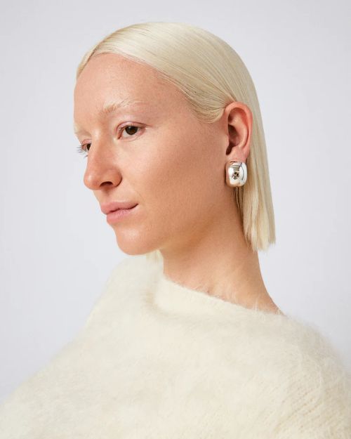 Head shot of a woman turning to the side to show her left ear with a small silver chunky silhouette earring.