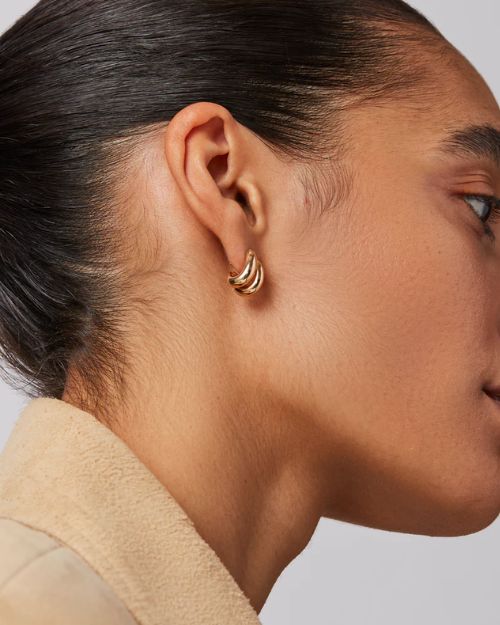 A woman's right-side profile of her ear focusing on the gold mini double stacked hoop earring she is wearing.