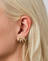 A woman's left-side profile of her ear focusing on her ear that is double pierced.  She is wearing two gold mini double stacked hoop earrings