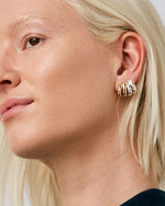 A woman's left-side profile of her ear focusing on her ear that is double pierced.  She is wearing two mini double stacked hoop earrings, one silver and one gold.