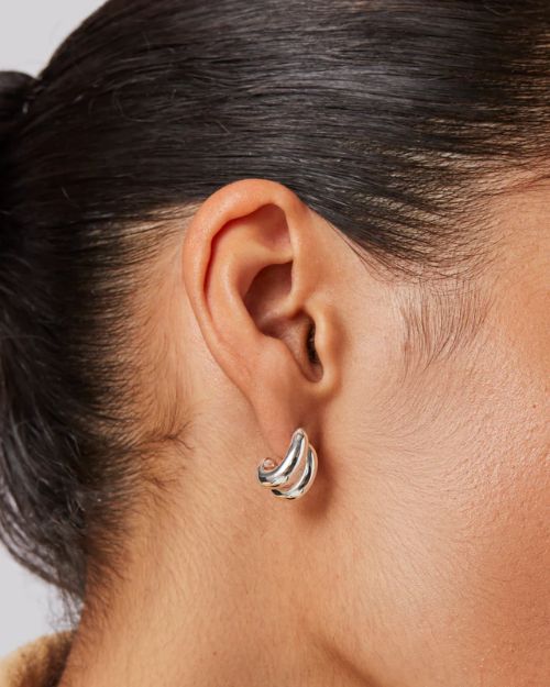 A woman's right-side profile of her ear up-close focusing on the silver small double stacked hoop earrings she is wearing. 
