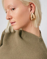 Head shot of a woman with only her left side showing wearing tear drop gold earrings. 