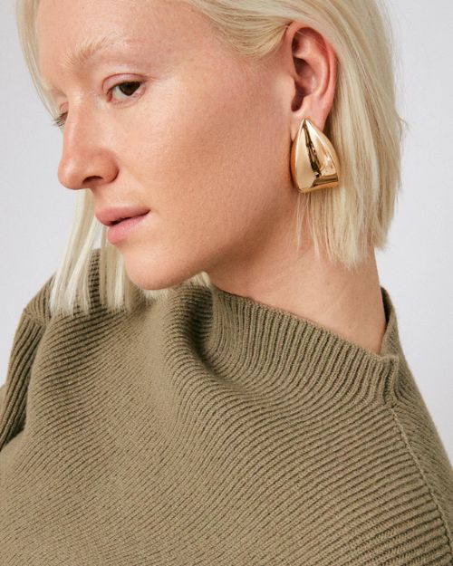 Head shot of a woman with only her left side showing wearing tear drop gold earrings. 