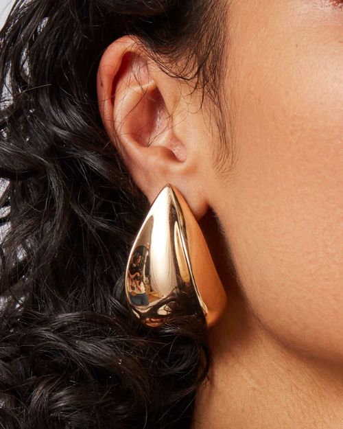 Up close image of a woman right ear and she is wearing a gold tear drop earring.