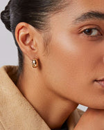 A woman's right-side profile of her ear up-close focusing on the thick small gold hoop she is wearing. 