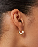 A woman's right-side profile of her ear focusing on the gold small thick earring she is wearing.