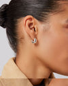 A woman's right-side profile of her ear focusing on the thick silver small hoop earring she is wearing.