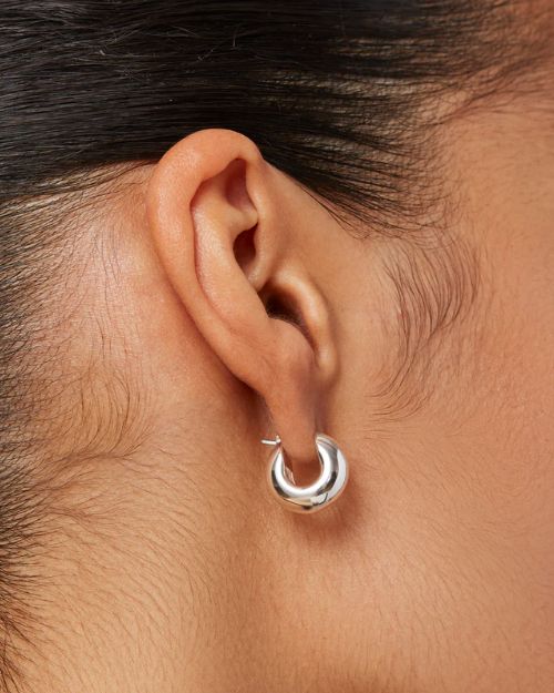 A woman's right-side profile of her ear up-close focusing on the thick small silver hoop she is wearing. 