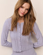 Close-up of a light lavender pointelle knit cardigan featuring a scalloped button-front closure, long sleeves, and delicate openwork detailing.