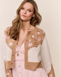 Close-up of a tan and cream patterned cardigan worn over a light pink dress, styled with a long gold pendant necklace.