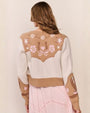 Back view of a person wearing a cropped tan and cream knit cardigan with star, floral, and horseshoe motifs, paired with a light pink dress.