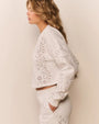 Side view of a white cropped sweatshirt with eyelet-style cutout patterns, paired with matching white bottoms.