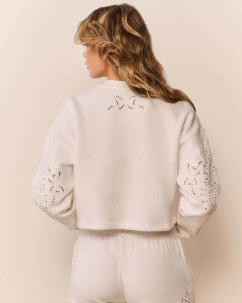Back view of a white cropped sweatshirt with eyelet cutout details on the sleeves and upper back, paired with matching white bottoms.