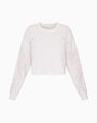 A white cropped sweatshirt with eyelet-style cutout detailing across the shoulders and sleeves, long sleeves with ribbed cuffs, and a relaxed fit.