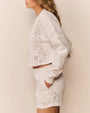 Side view of a white cropped sweatshirt and matching shorts set both featuring eyelet-style cutout patterns