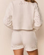 Back view of a white cropped sweatshirt and matching shorts with eyelet-style cutout details