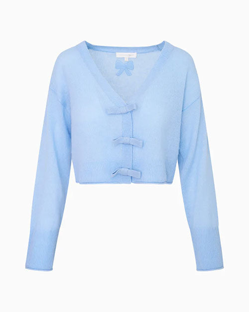 A light blue cropped cardigan sweater set up in front of a white background, showcasing thin bows down the front for closure, and a bow design adorned on the back under the neckline. 