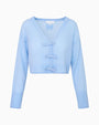 A light blue cropped cardigan sweater set up in front of a white background, showcasing thin bows down the front for closure, and a bow design adorned on the back under the neckline. 