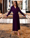Model wearing purple long dress with long sleeves in a fancy hotel background.
