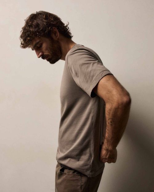 A side view of a man dressed in a Brushed Lotus Crew t-shirt and jeans poses in a casual setting, highlighting a laid-back fashion choice.