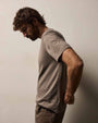 A side view of a man dressed in a Brushed Lotus Crew t-shirt and jeans poses in a casual setting, highlighting a laid-back fashion choice.