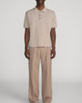 Beige short-sleeve polo shirt paired with matching straight-leg trousers, featuring a relaxed fit and clean minimalist styling on a light grey background.