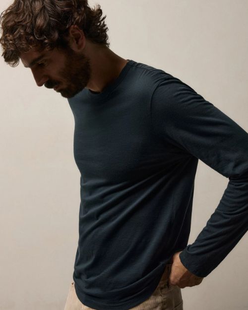 A man wearing a navy long sleeve crew shirt and khaki pants stands confidently.
