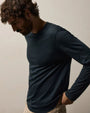 A man wearing a navy long sleeve crew shirt and khaki pants stands confidently.
