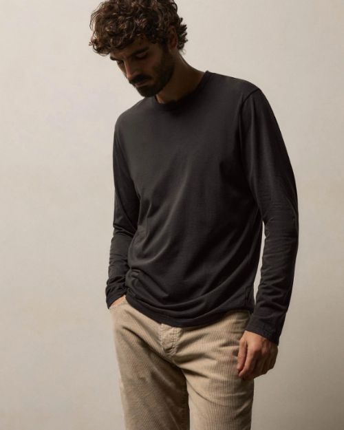 A man in a long sleeve shirt and khaki pants stands, showcasing a relaxed and stylish look.