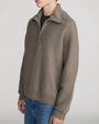 Taupe zip-neck knit sweater featuring a high collar, long sleeves, and a relaxed fit, styled with blue denim jeans on a light grey background.