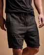  A man dressed in black linen shorts and a matching black shirt, exuding a relaxed and stylish vibe.