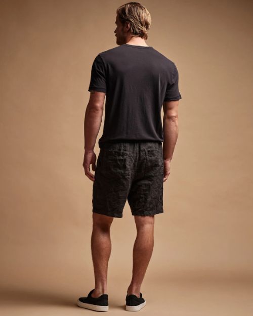 A man dressed in black linen shorts and a black t-shirt poses casually.