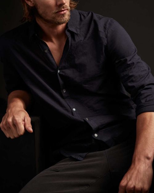 A man with long hair wearing a cotton button-up shirt.