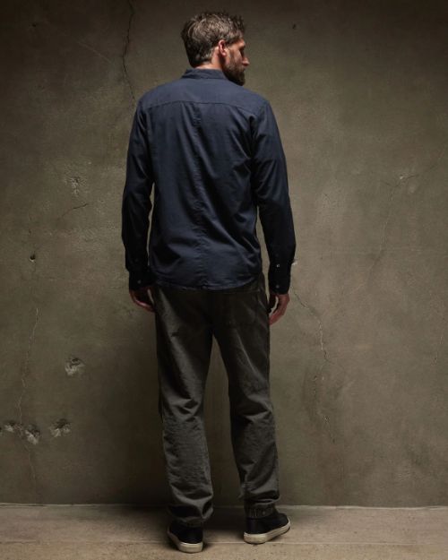 The back view of a man with a beard wearing a cotton button-up shirt, standing in a relaxed pose.