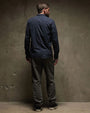 The back view of a man with a beard wearing a cotton button-up shirt, standing in a relaxed pose.