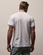Back view of a white crew neck T-shirt featuring a classic short-sleeve design and relaxed fit, styled with light wash denim jeans on a neutral studio background.