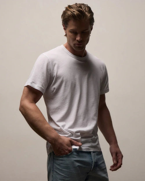 White crew neck T-shirt featuring a classic short-sleeve design and relaxed fit, styled with light wash denim jeans on a neutral studio background.