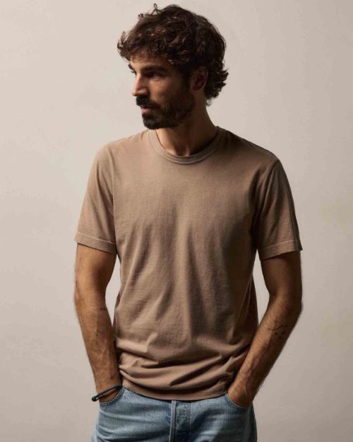 A man wearing a coffee color cotton crew neck t-shirt and jeans stands casually.