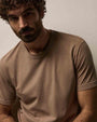 A man with curly hair wearing a coffee color 100% cotton crew neck t-shirt, smiling at the camera.
