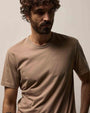 A man with curly hair wearing a coffee color 100% cotton crew neck short sleeve t-shirt.